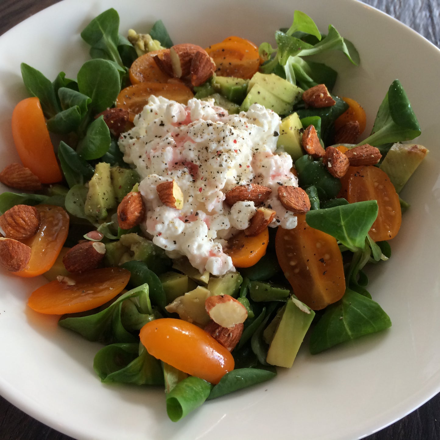 Salade met veldsla, avocado, amandelen, oranje tomaatjes en hüttenkäse